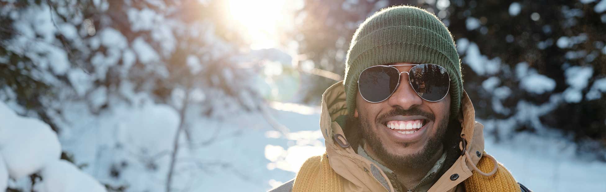 A smiling male international student wearing a warm coat and sunglasses, enjoying his first Canadian winter.