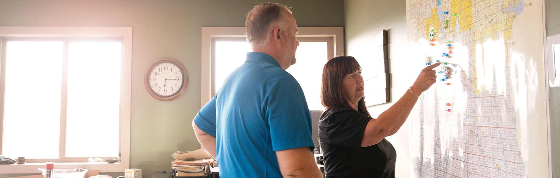 A female arm manager in her office pointing to an aerial map of the farm, discussing strategy with a male employee.
