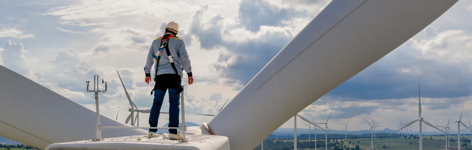A wind turbine technician stands on top of a wind turbine