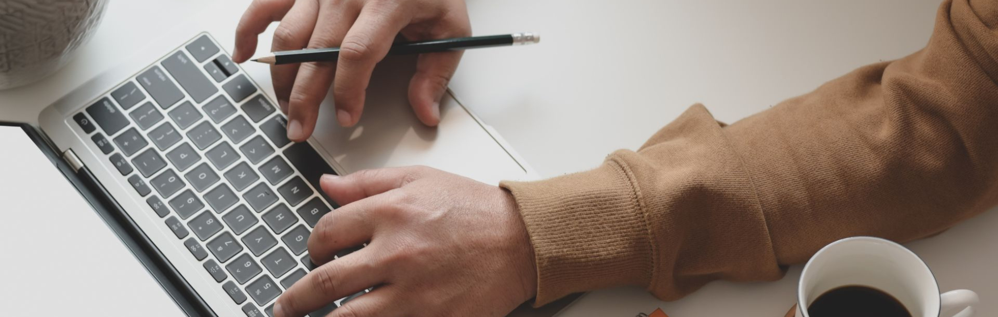 A hand holding a pencil while navigating the mouse pad on the laptop