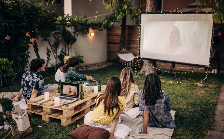 Group of friends watching a movie on projector in a garden.