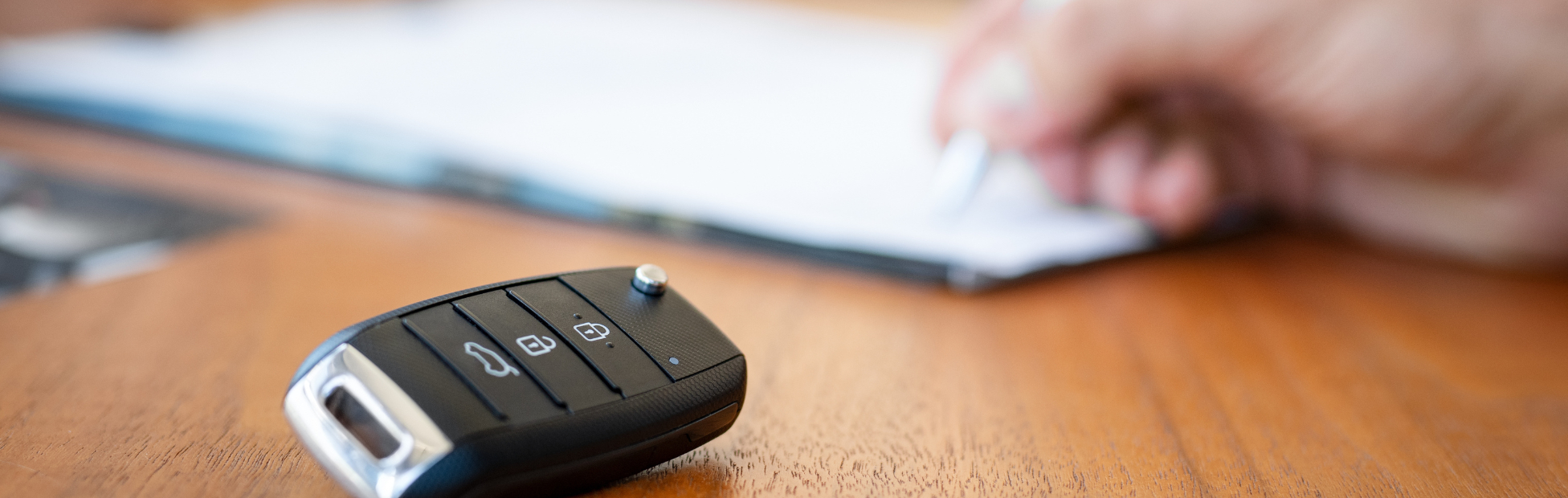 Visible hand at a desk signing an agreement with car keys in the foreground