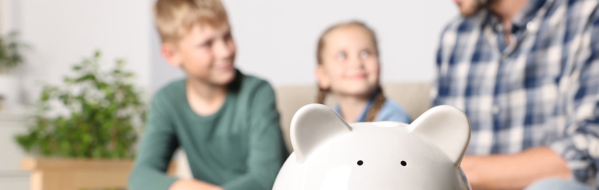 A father with his son & daughter with a piggy bank in focus in the foreground