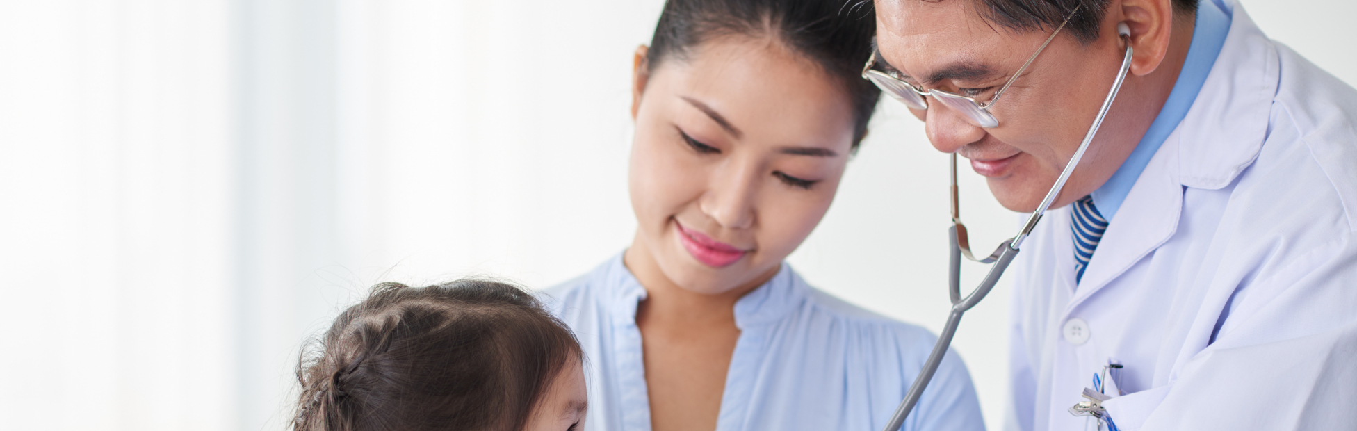 Young Asian girl and her mom looking at pediatrician while he examines her