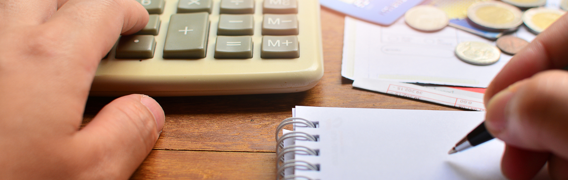 Hand on a calculator with credit cards and Canadian coins blurred in the background