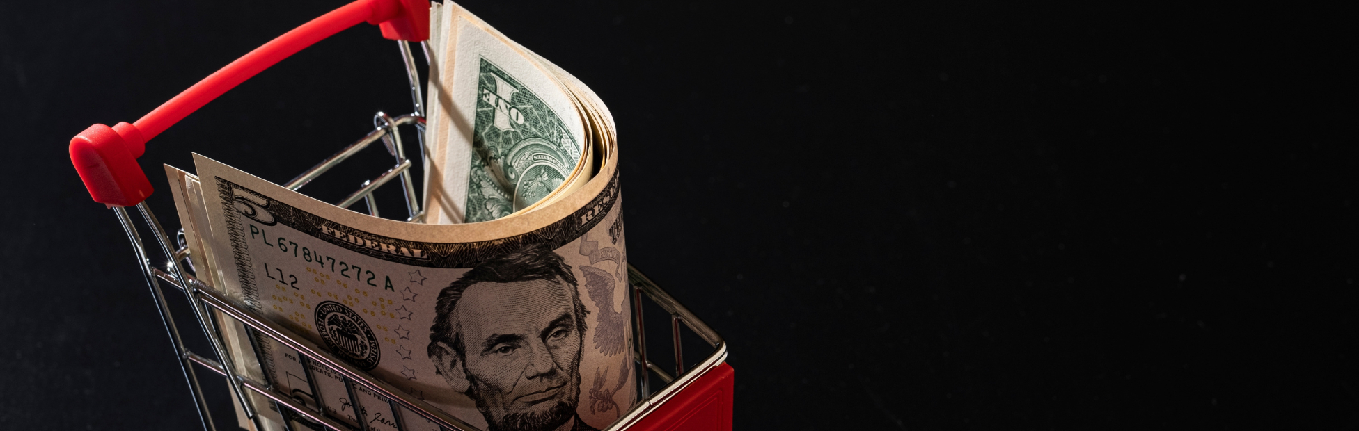 Miniature shopping cart on a black background filled with US dollars