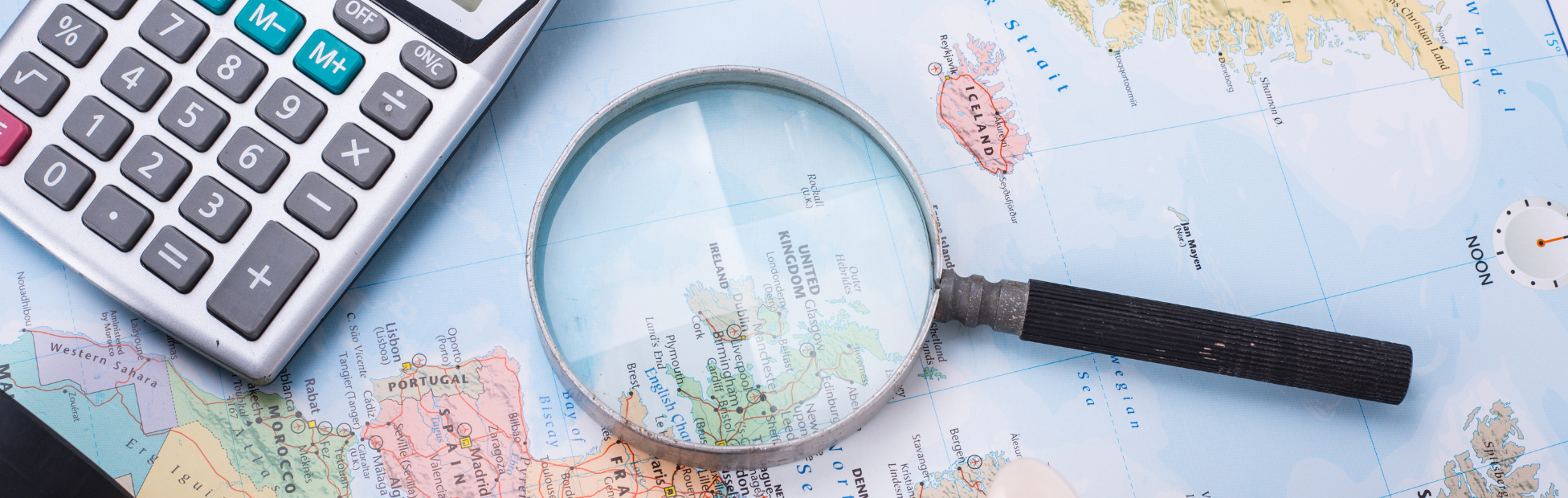 Map of the world with magnifying glass, piggy bank and calculator sitting on top