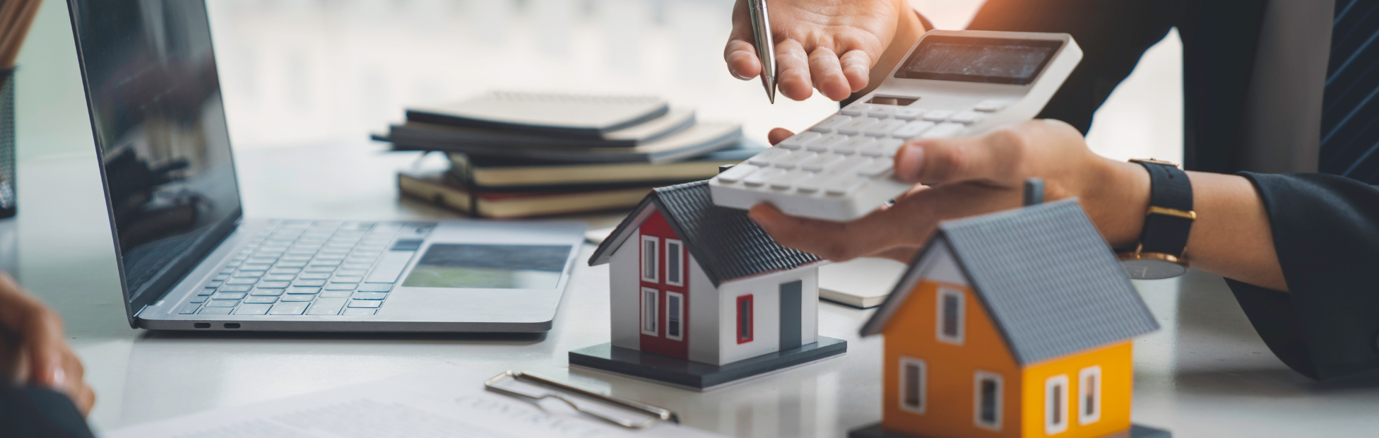 Out of focus woman at a desk with a calcultor, paperwork and two toy houses
