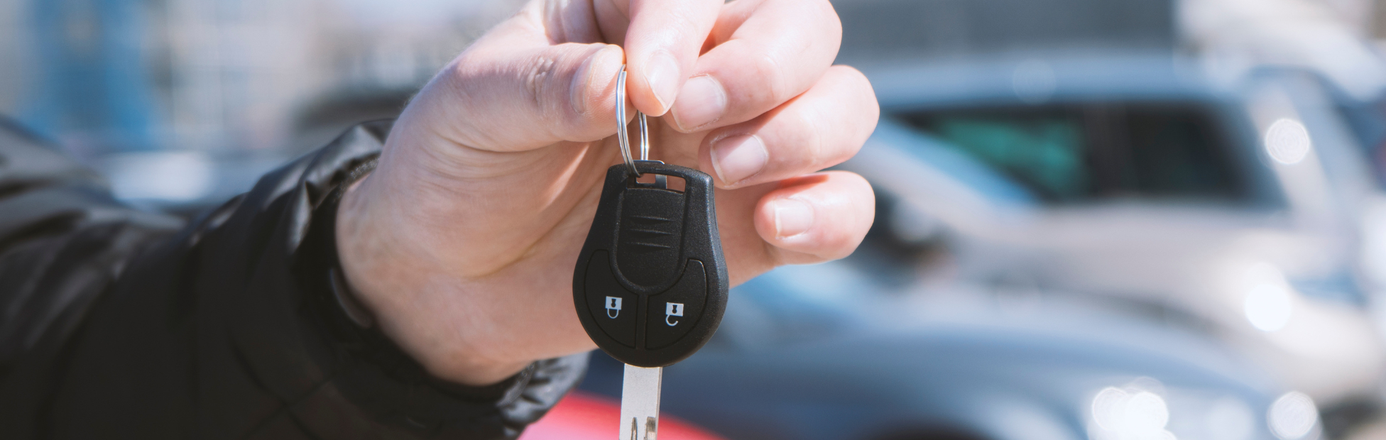 Out of focus car lot with a male hand holding a car key in the foreground