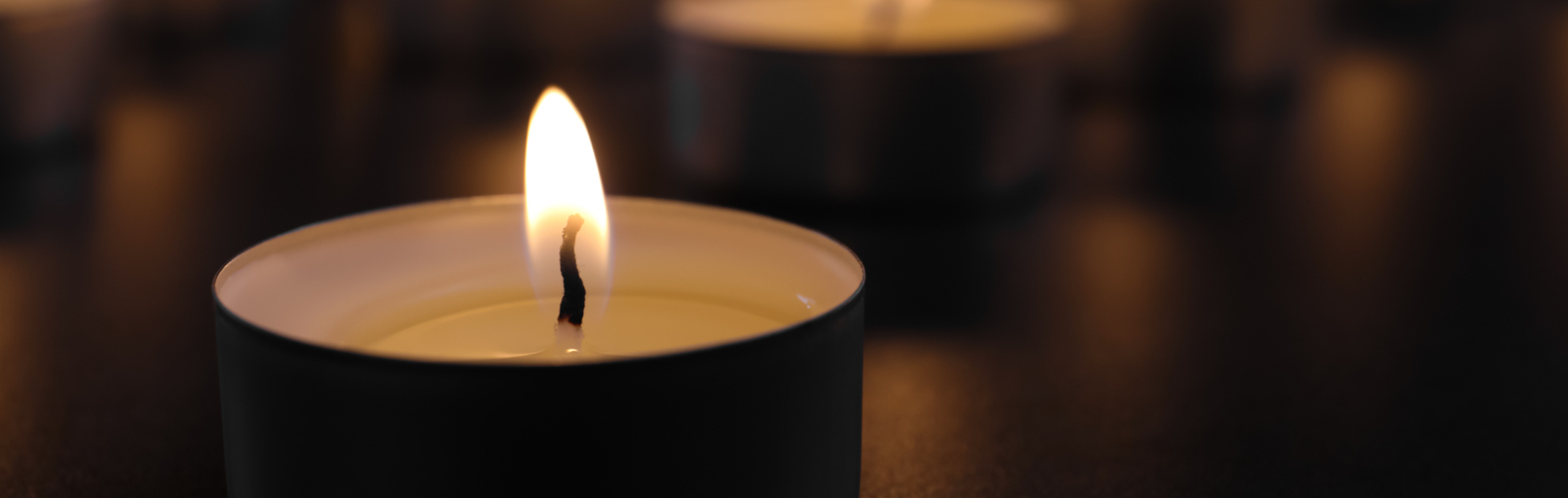 Burning candle on table in darkness