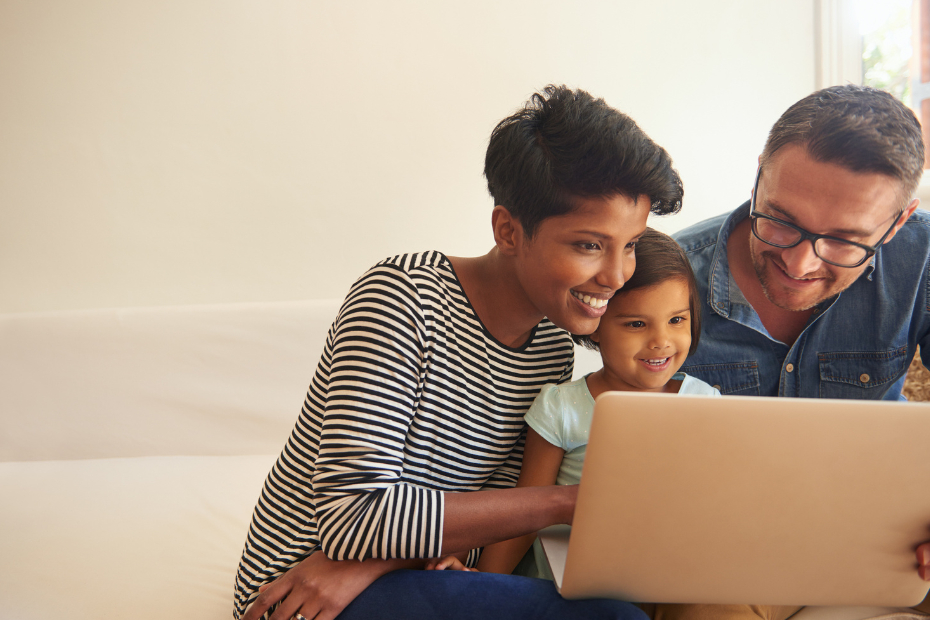 A smiling mother, daughter and father, looking at a laptop