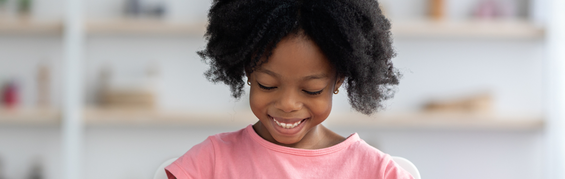 Happy young African American girl in bright pink shirt, playing with colorful wooden blocks