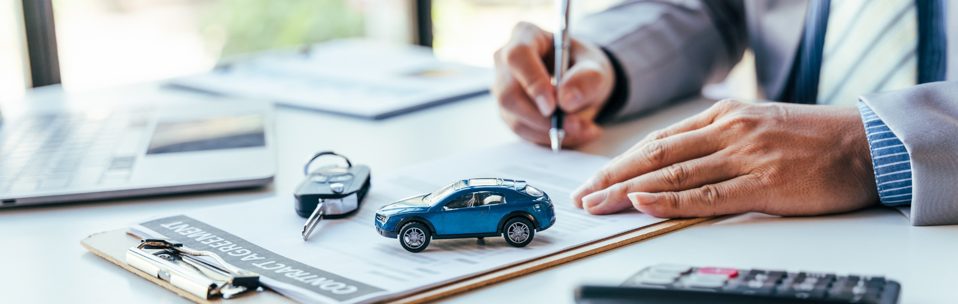 Man signing car loan paperwork with calculator beside him on a desk