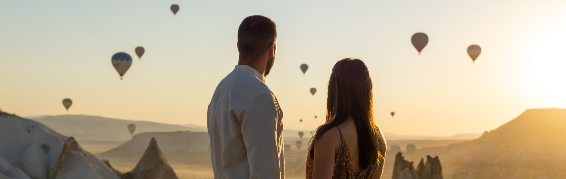 Young Couple holding hands looking at the sun setting over the mountains