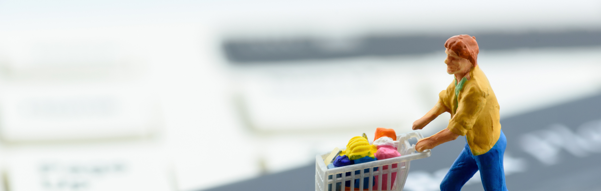 Miniature figurine shopper pushing a shopping cart on a smart credit card and a keyboard.