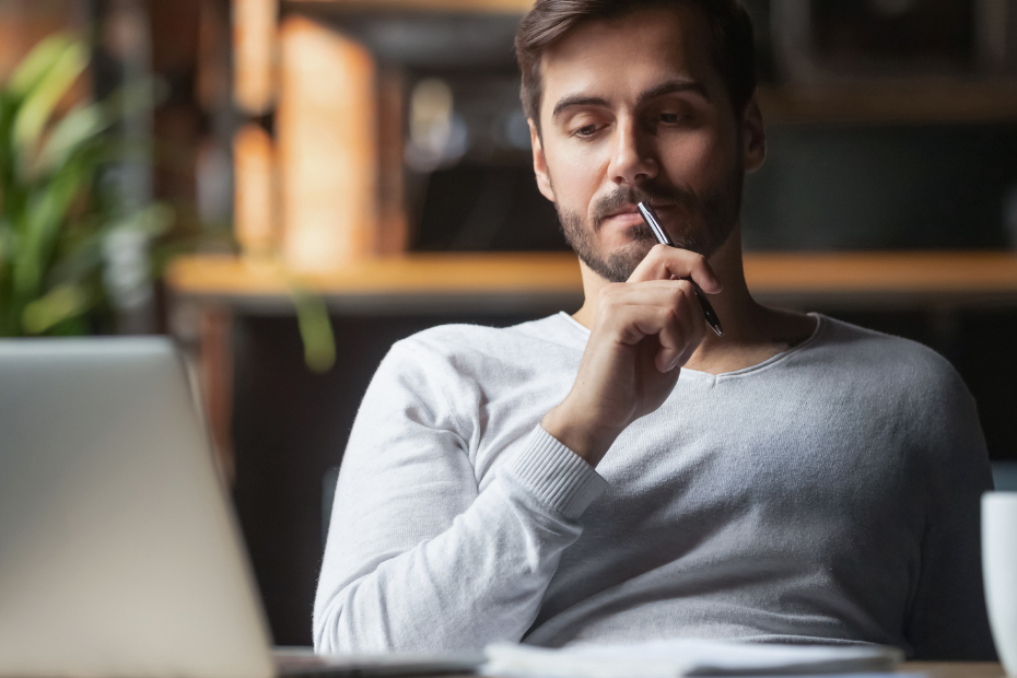 Pensive bearded man sitting at desk drinking coffee