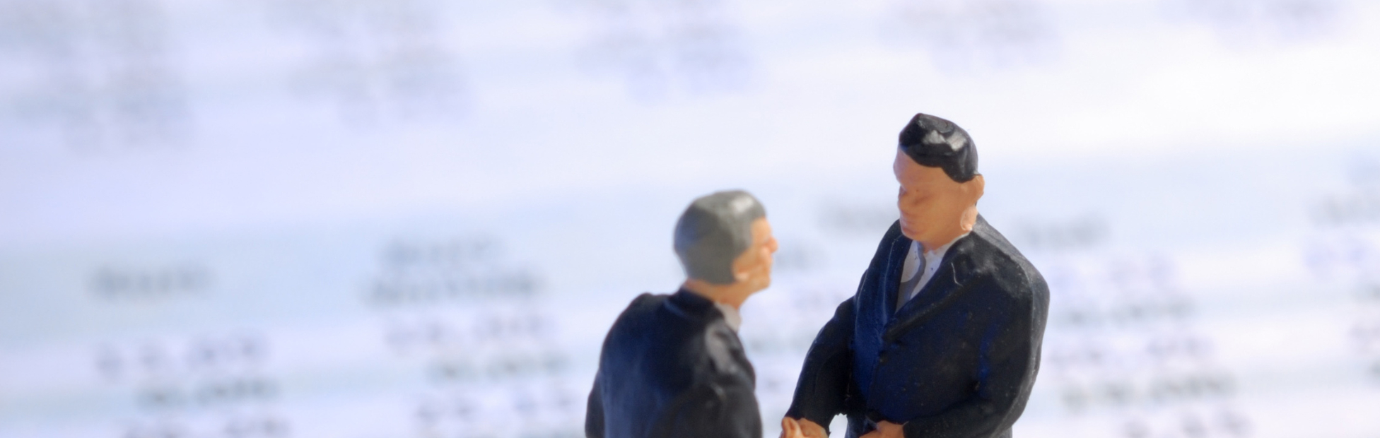 Two grey-haired miniature model figures standing on life-sized spreadsheets