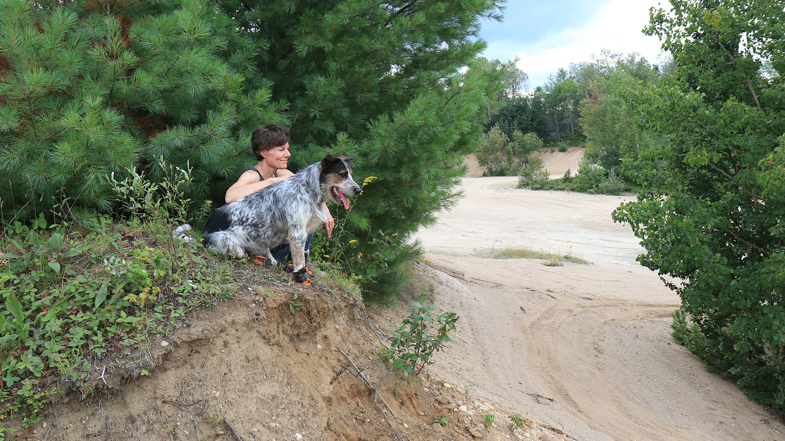 Muttluks founder Marianne Bertrand with a grey spotted dog sitting under a tree 