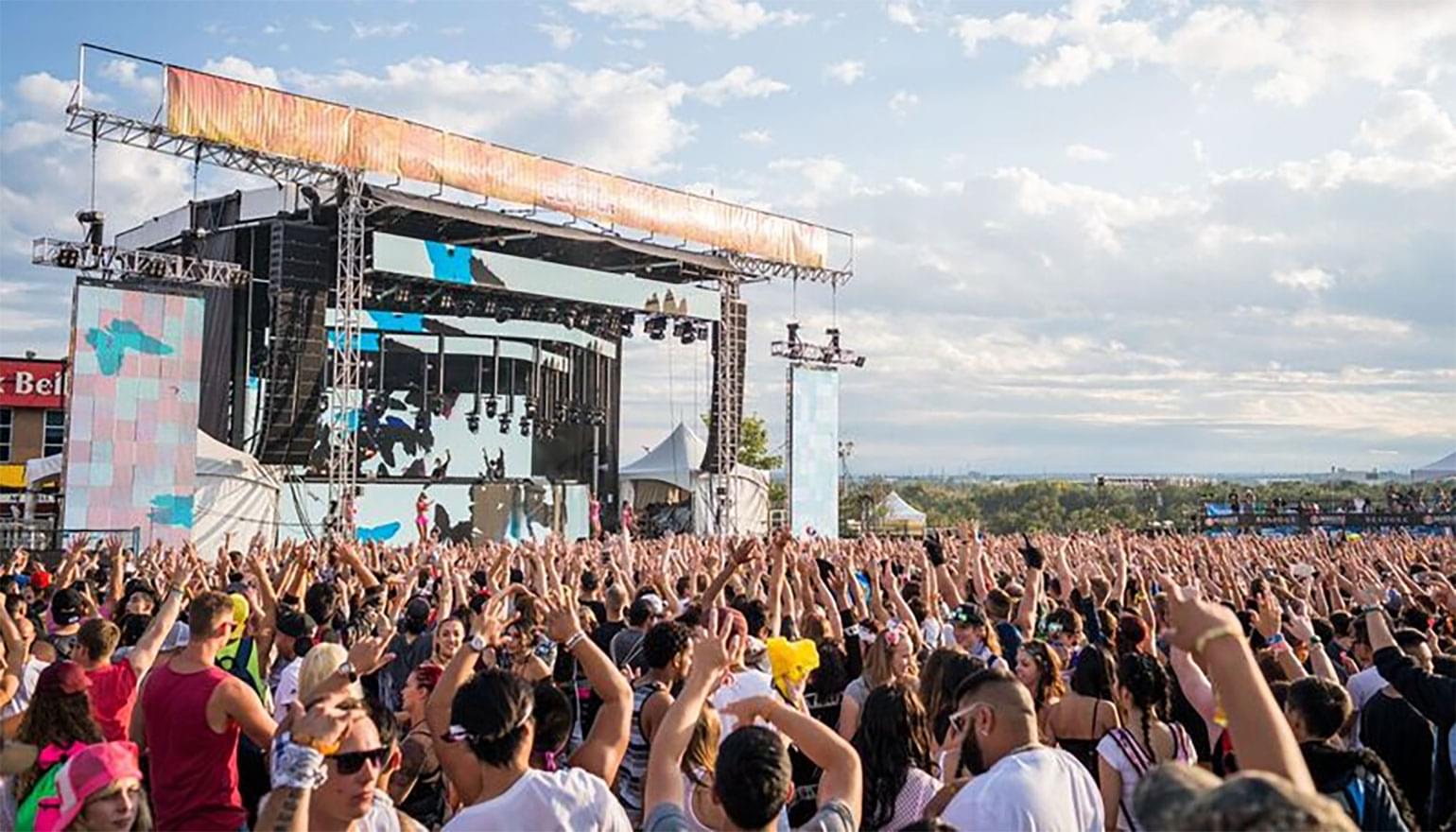 Large crowd at a festival with hands in the air.