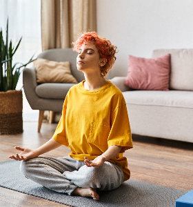 Beautiful extravagant queer person with red hair in vibrant yellow t shirt meditating at home