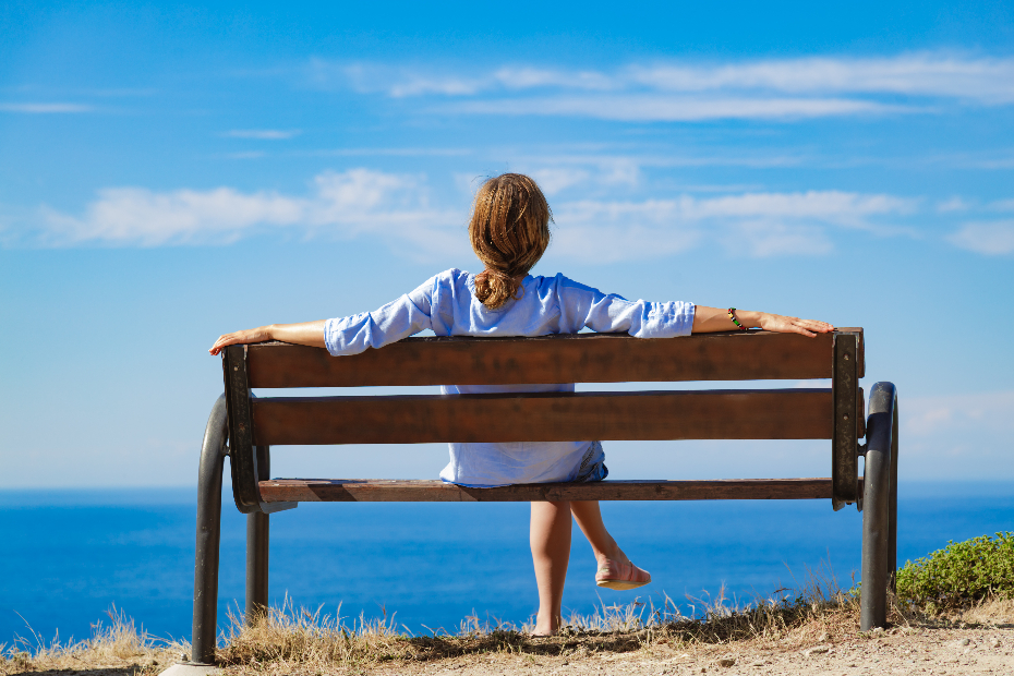 Woman contently sitting on a bench overlooking the ocean