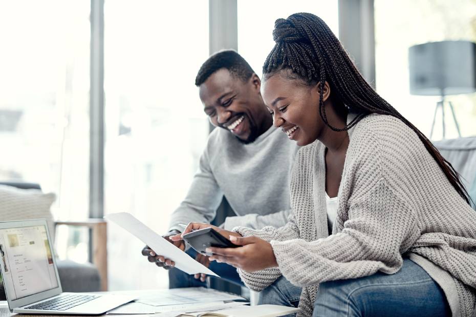 A smiling Black couple sitting on a white couch, reviewing mortgage payment options on a tablet