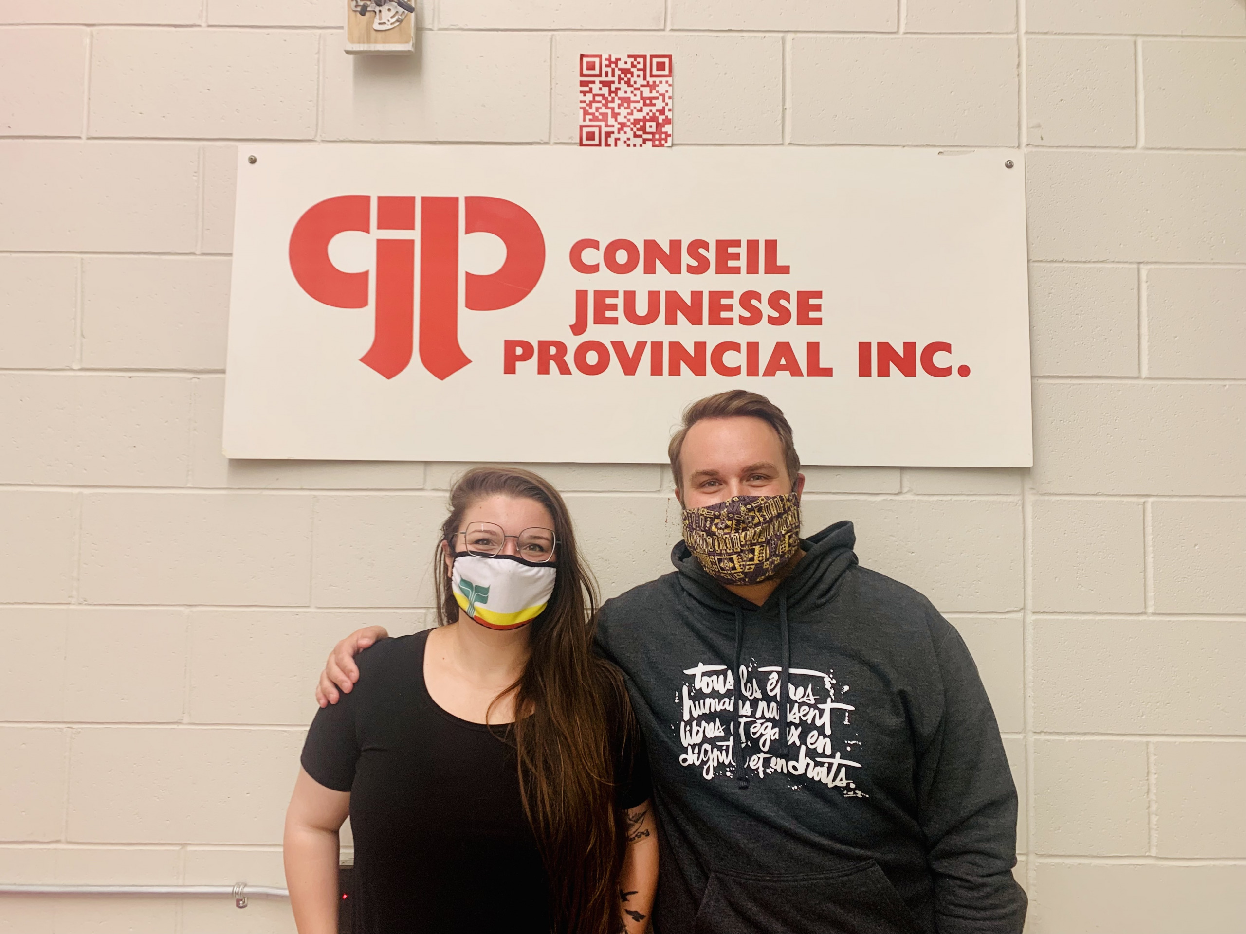 A photo of José Roy and Derrek Bentley in front of the Conseil jeunesse provincial sign. 